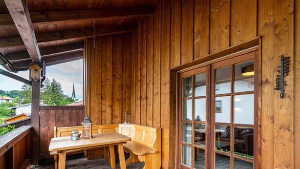 Une cabane en bois avec une table et un banc en bois, une grande porte vitrée et une rambarde en bois.
