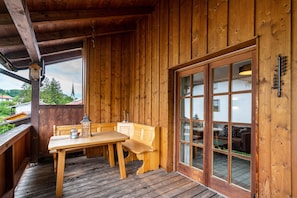 Une cabane en bois avec une table et un banc en bois, une grande porte vitrée et une rambarde en bois.