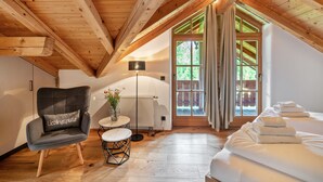 Une chambre confortable située dans les combles, avec des poutres en bois, une chaise, une petite table, un radiateur et un lit avec des serviettes.