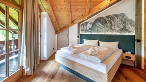 Une chambre avec un plafond en bois, un lit recouvert de draps blancs, une table de chevet et une grande fenêtre avec des rideaux.