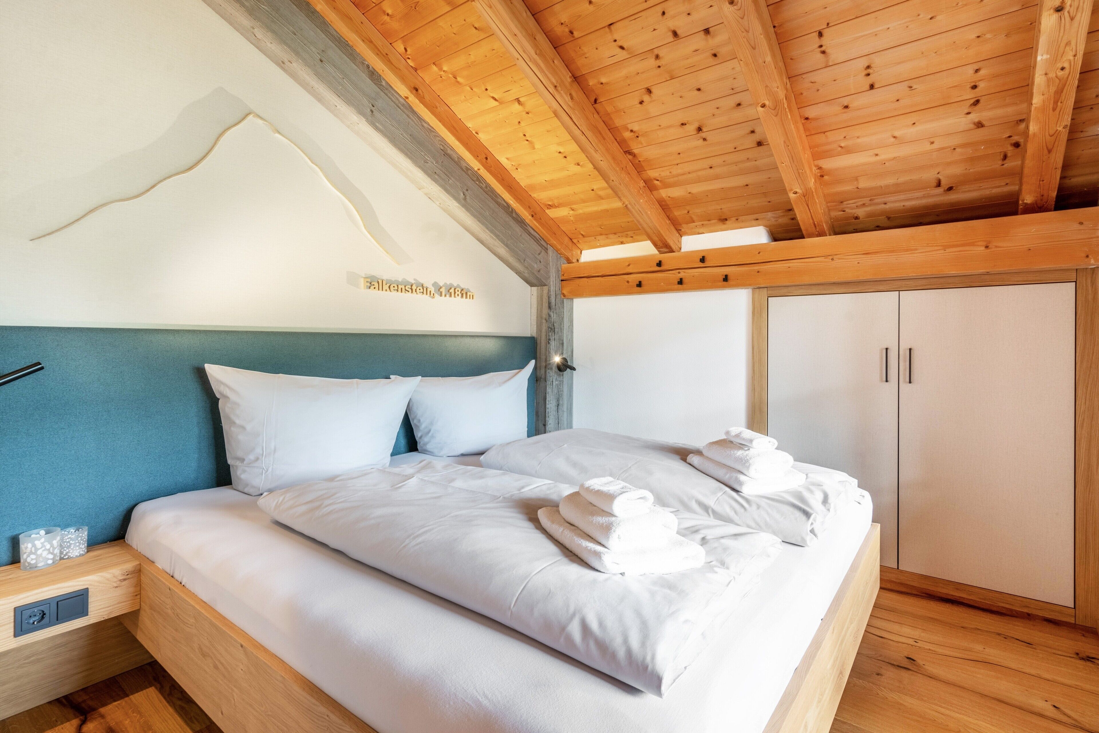 A bedroom with a bed, nightstand, wardrobe, and wooden ceiling beams.