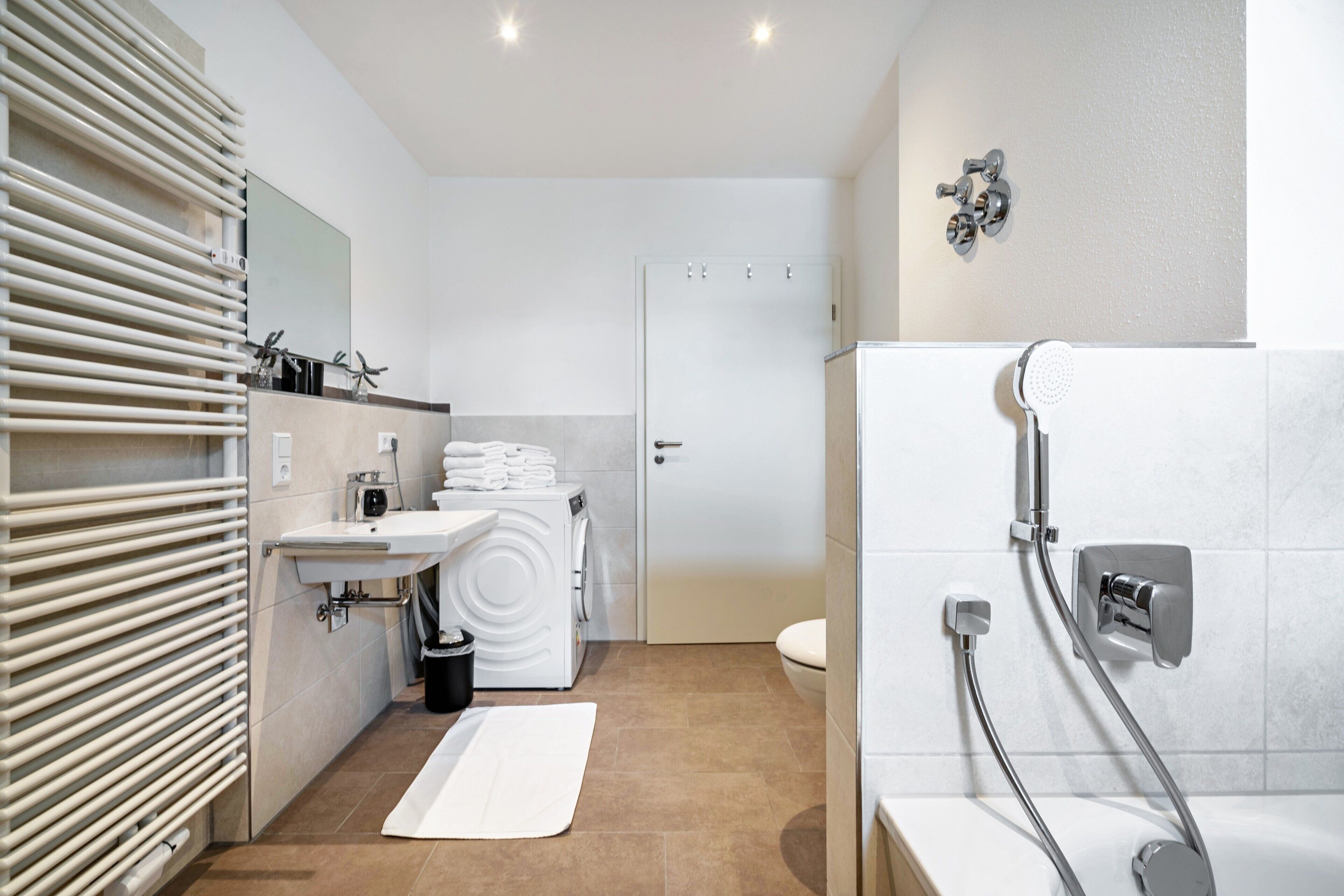 A modern bathroom with a sink, mirror, towel rack, shower, and a door leading to another room.