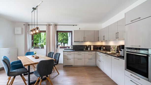 A modern kitchen with white cabinets, a dining table with chairs, and a built-in oven. - Apartment 'Haus Katharina 2' with Mountain View, Private Terrace and Wi-Fi (Inzell)