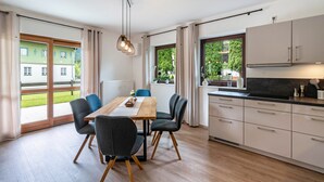 A modern kitchen with a dining area, large windows, and a view of a green building outside. - Apartment 'Haus Katharina 2' with Mountain View, Private Terrace and Wi-Fi (Inzell)