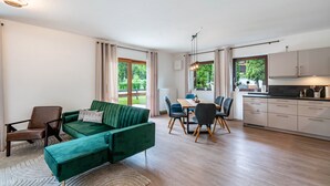 A modern living room with a green sofa, dining table, and kitchen area. - Apartment 'Haus Katharina 2' with Mountain View, Private Terrace and Wi-Fi (Inzell)