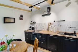 Une cuisine moderne avec des poutres en bois, un îlot central, des meubles de couleur noire et un revêtement mural blanc.