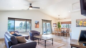 A spacious living room with a leather sofa, a coffee table, and a dining area with a chandelier. - Dark Sky Retreat Near Sedona • Hot Tub, Sauna & Mountain Views (Cornville)
