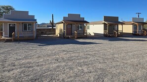 A row of small, single-story cabins with wooden exteriors and simple designs, arranged in a gravel lot with a clear blue sky above. - Wild West Cabin Suite (Quartzsite)
