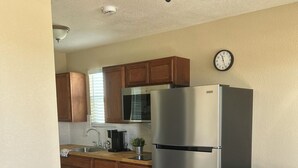 A compact kitchen with wooden cabinets, a stainless steel refrigerator, a dining table with chairs, and a black sofa with patterned cushions. - Wild West Cabin Suite (Quartzsite)