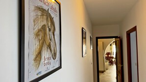 A hallway with a framed horse painting on the wall, a door at the end, and a light fixture above. - Apartamento Las Palmeras - Ole Solutions (Jerez de la Frontera)