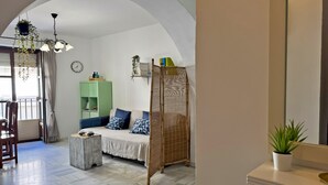 A spacious living area with a sofa, a dining table, and a hanging plant. - Apartamento Las Palmeras - Ole Solutions (Jerez de la Frontera)