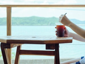 Une table en bois, avec une boisson et un stylo, donnant sur une étendue d’eau et une zone verdoyante.