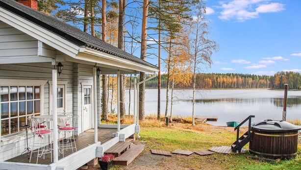 Una baita con veranda, vasca idromassaggio e vista su un lago circondato da alberi.