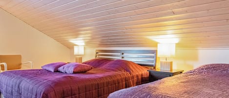 A bedroom with two beds, wooden ceiling, and bedside lamps.