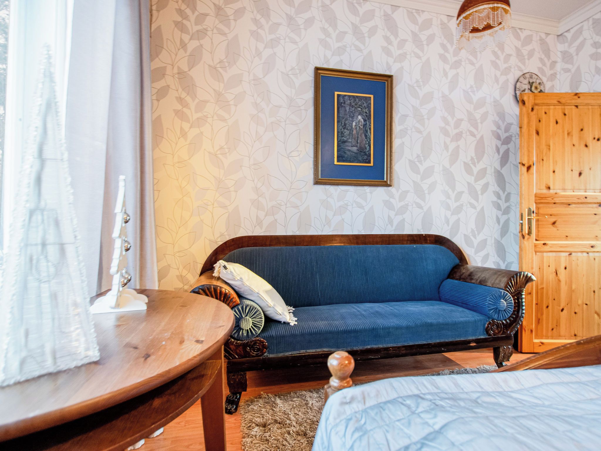 Una habitación con un sofá azul, un armario de madera, un cuadro en la pared y una ventana con cortinas.