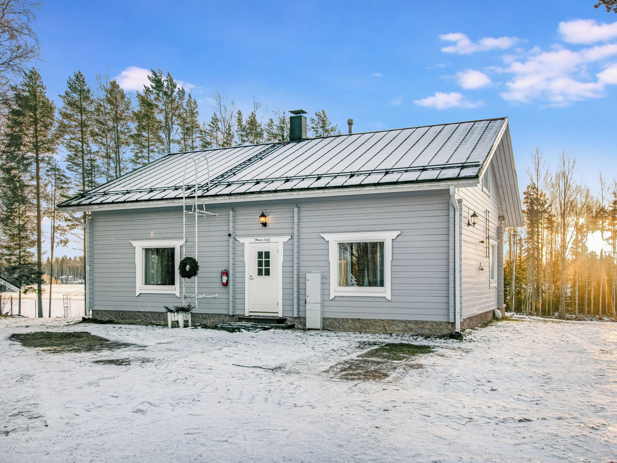 Une cabane de plain-pied avec un toit en métal, un revêtement extérieur blanc et une porte d’entrée.