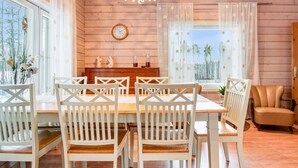 Zona pranzo con tavolo in legno e sedie bianche, un lampadario e vista sugli alberi attraverso ampie finestre.