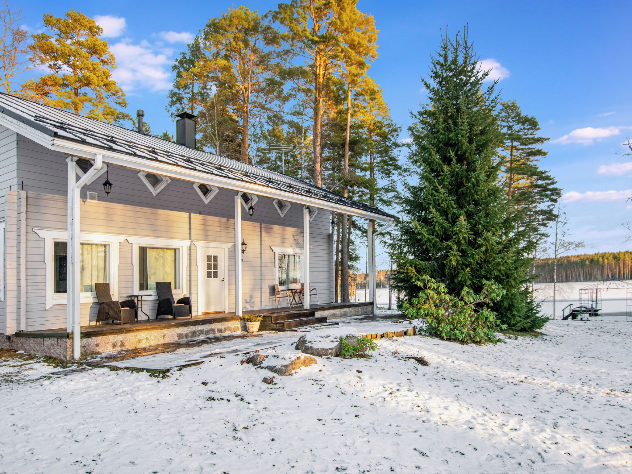 A house with a covered porch, outdoor seating, and a snow-covered yard.