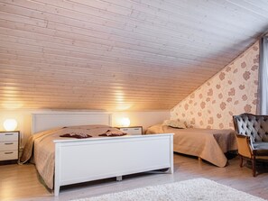 A bedroom with a sloped ceiling, a bed with a headboard, bedside tables, a chair, and patterned wallpaper. - Mänty-linna by Interhome (Kihniö)