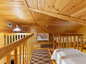Interior de cabana de madeira com quarto no mezanino, pequena cozinha e guarda-corpo de madeira.