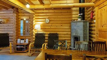A log cabin interior with a wooden dining table, chairs, a fireplace, and a clock on the wall.