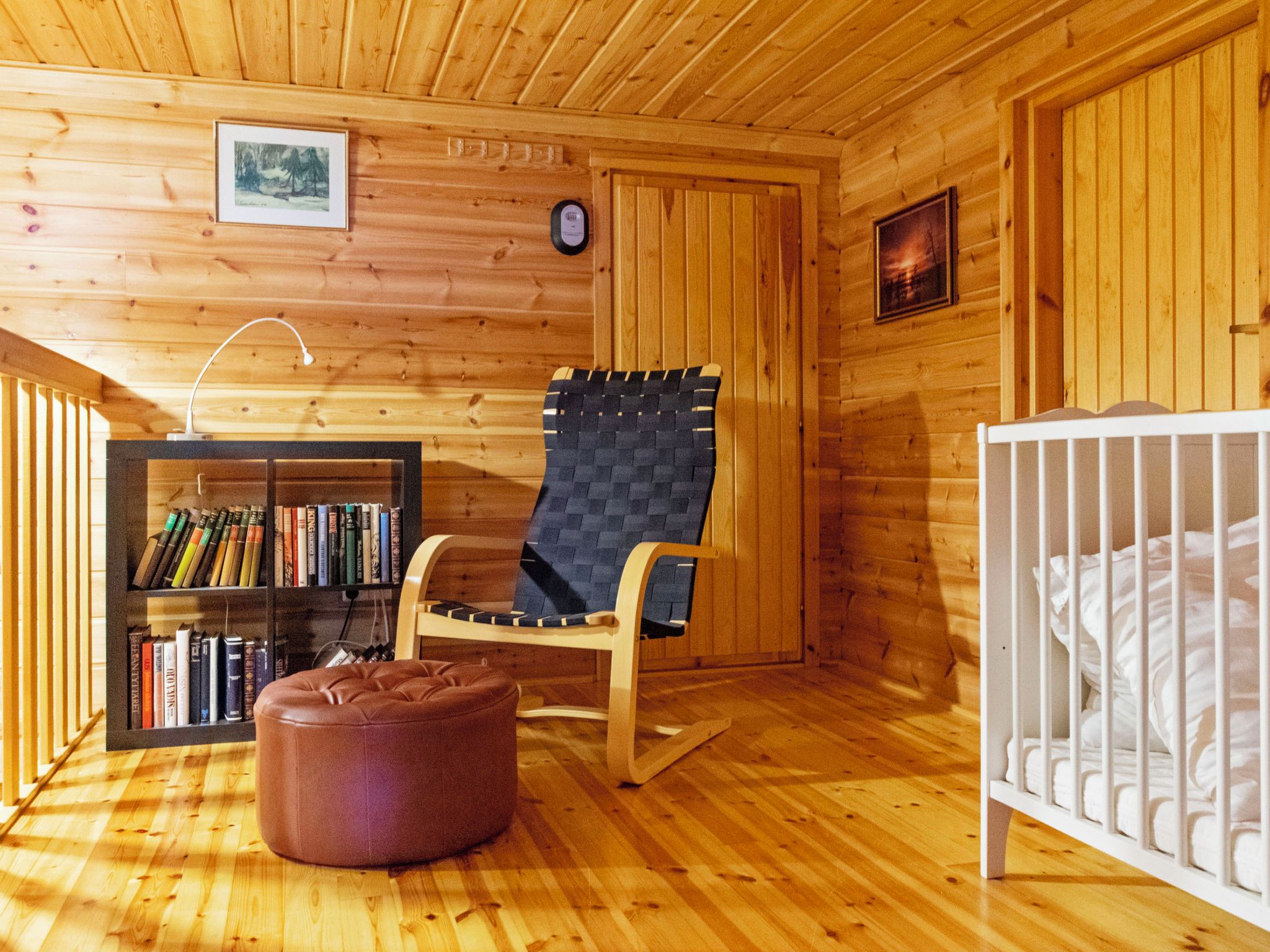 Een houten cabin met een schommelstoel, een boekenkast, een ledikant en een houten plafond.