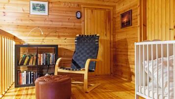 Een houten cabin met een schommelstoel, een boekenkast, een ledikant en een houten plafond.