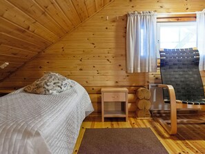 Une chambre confortable dans un chalet en bois, avec un lit, une table de chevet, une chaise et une fenêtre avec des rideaux.