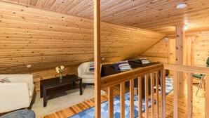 Interior acogedor de una cabaña de madera con cama en altillo, un sofá, una mesita y un jarrón decorativo.