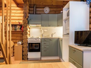 A compact kitchen with a stove, sink, and cabinets, and a television on the right.