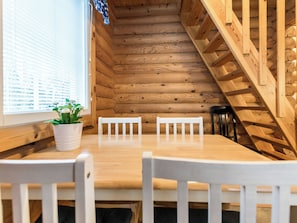 Un interior de madera con una mesa de comedor y sillas, una ventana con persianas, y una escalera.