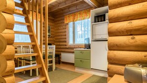 Ein rustikales Blockhaus mit einer Holztreppe, einer Küchenzeile inklusive Mikrowelle und Kühlschrank sowie einem Esstisch mit Stühlen.