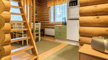 Ein Holzblockhaus-Interieur mit einer Holztreppe, einem Essbereich mit Stühlen, einer Küche mit Kühlschrank und einem Fenster mit Vorhängen.