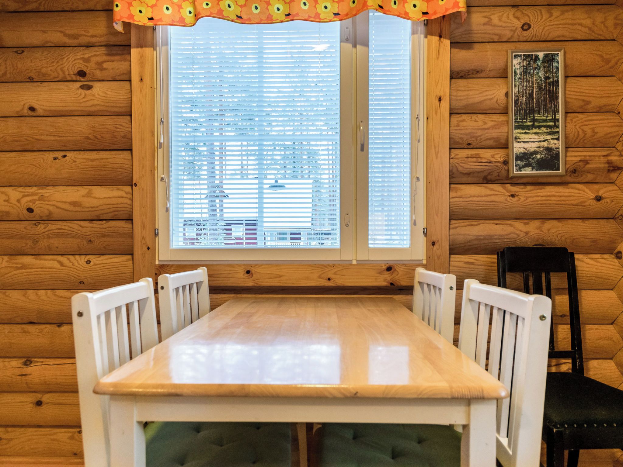 Eine Holzhütte mit einem Esstisch und Stühlen, einem Fenster mit Jalousien und einem gerahmten Bild an der Wand.