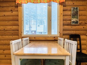 Una cabaña de madera con una mesa de comedor y sillas, una ventana con persianas y un cuadro en la pared.