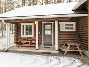 A log cabin with a porch, two windows, a door, and a small table.