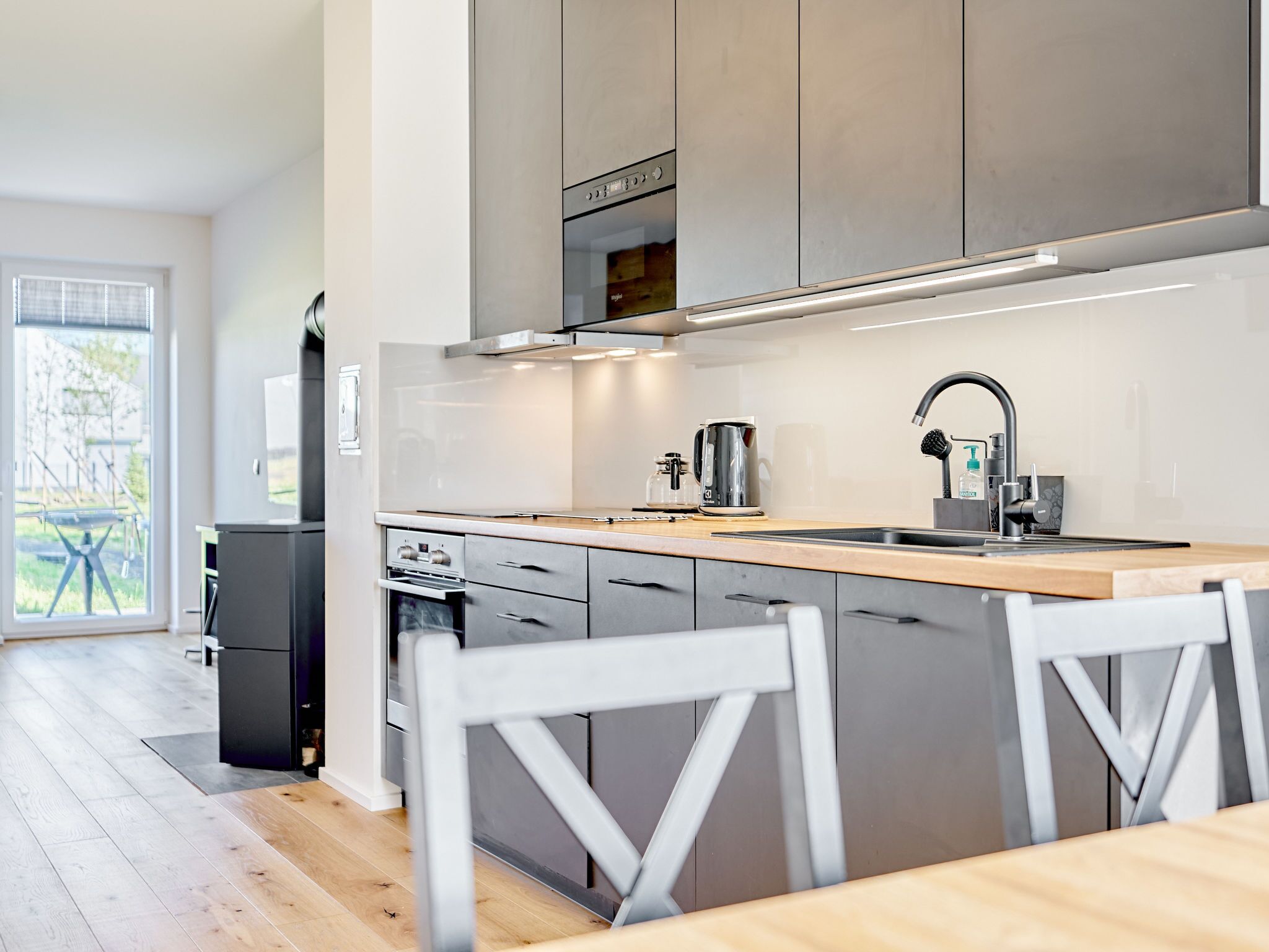 Une cuisine moderne avec des meubles gris, un plan de travail en bois et un évier en acier inoxydable.