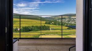 Un balcon donnant sur une vallée verdoyante et sur des bâtiments situés au loin.