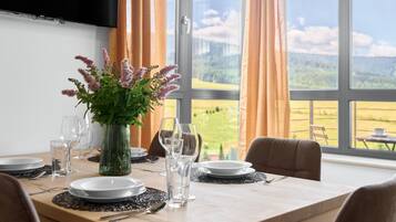 Een eettafel gedekt met borden, glazen en een bloevas, met uitzicht op een landschap door grote ramen.