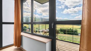Een kamer met een groot raam, uitzicht op een groen landschap en een heldere lucht.