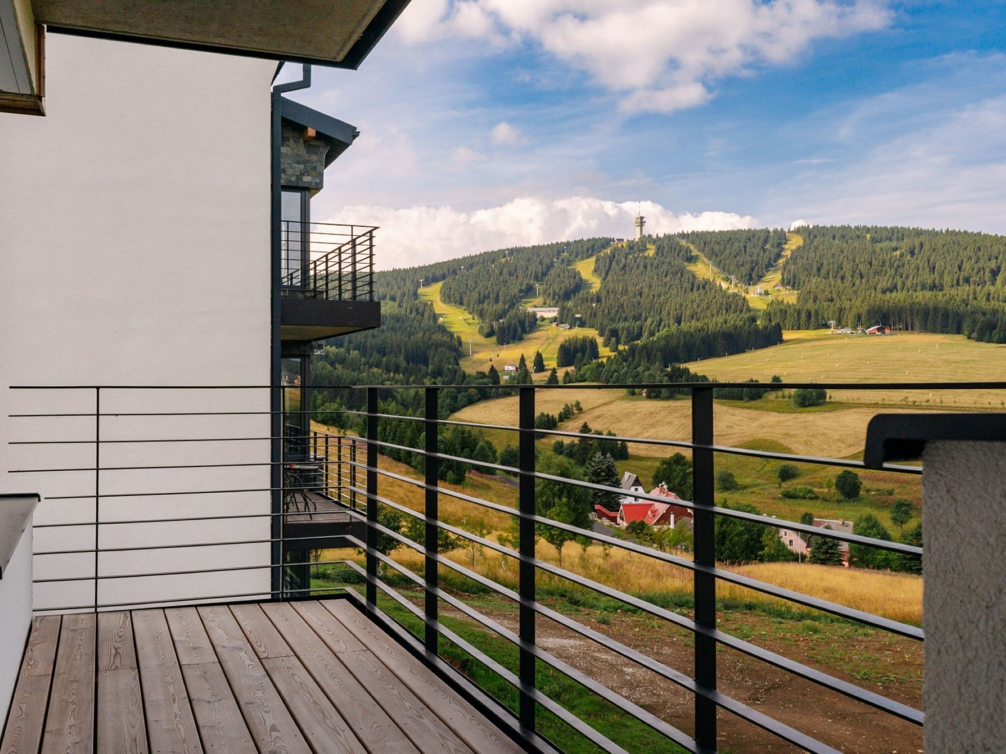 Uma varanda com vista para uma paisagem montanhosa, um deck de madeira e um corrimão de metal.