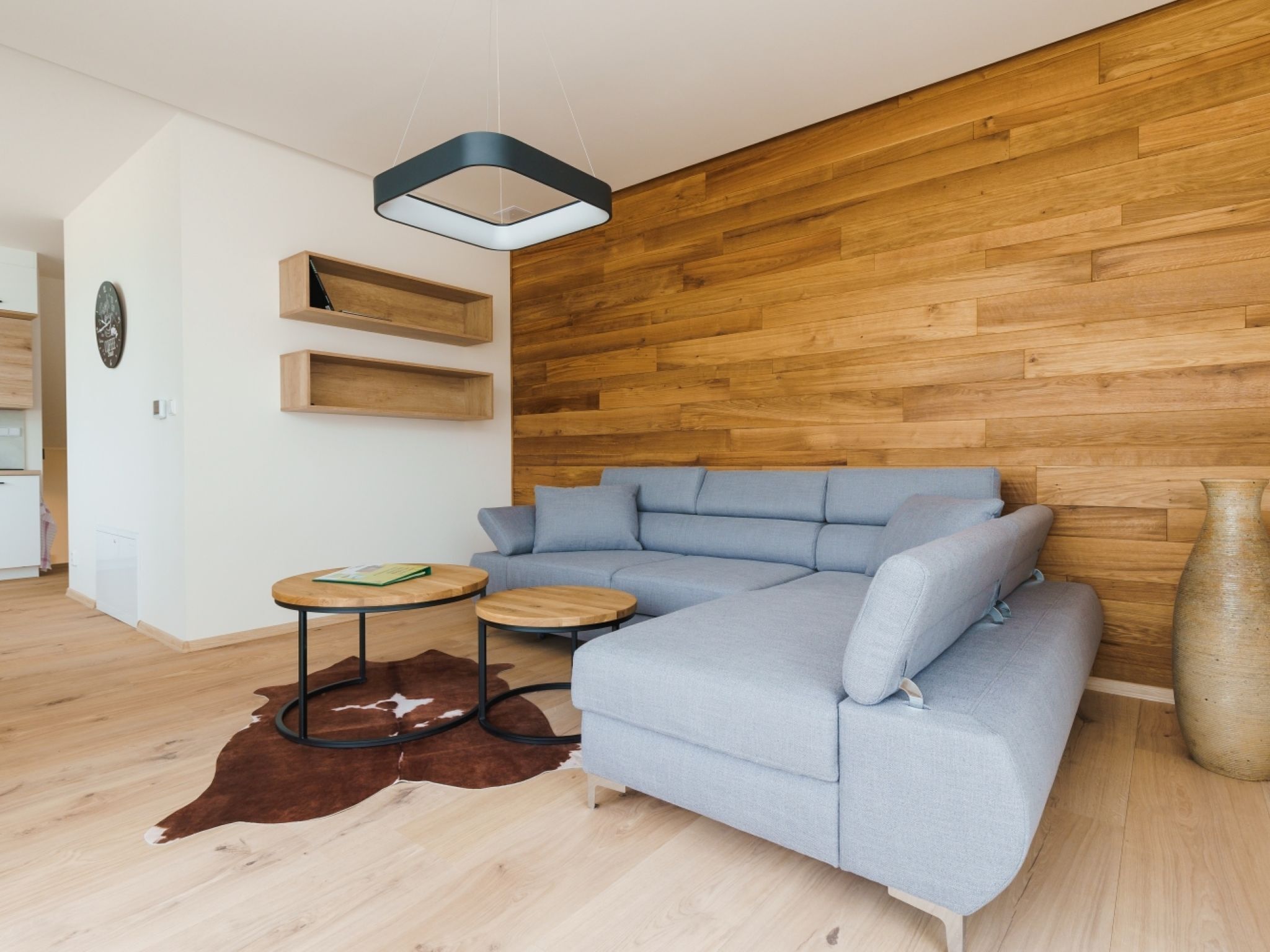 Een moderne woonkamer met een lichtblauwe modulaire bank, een ronde houten salontafel en een koperen vloerkleed.