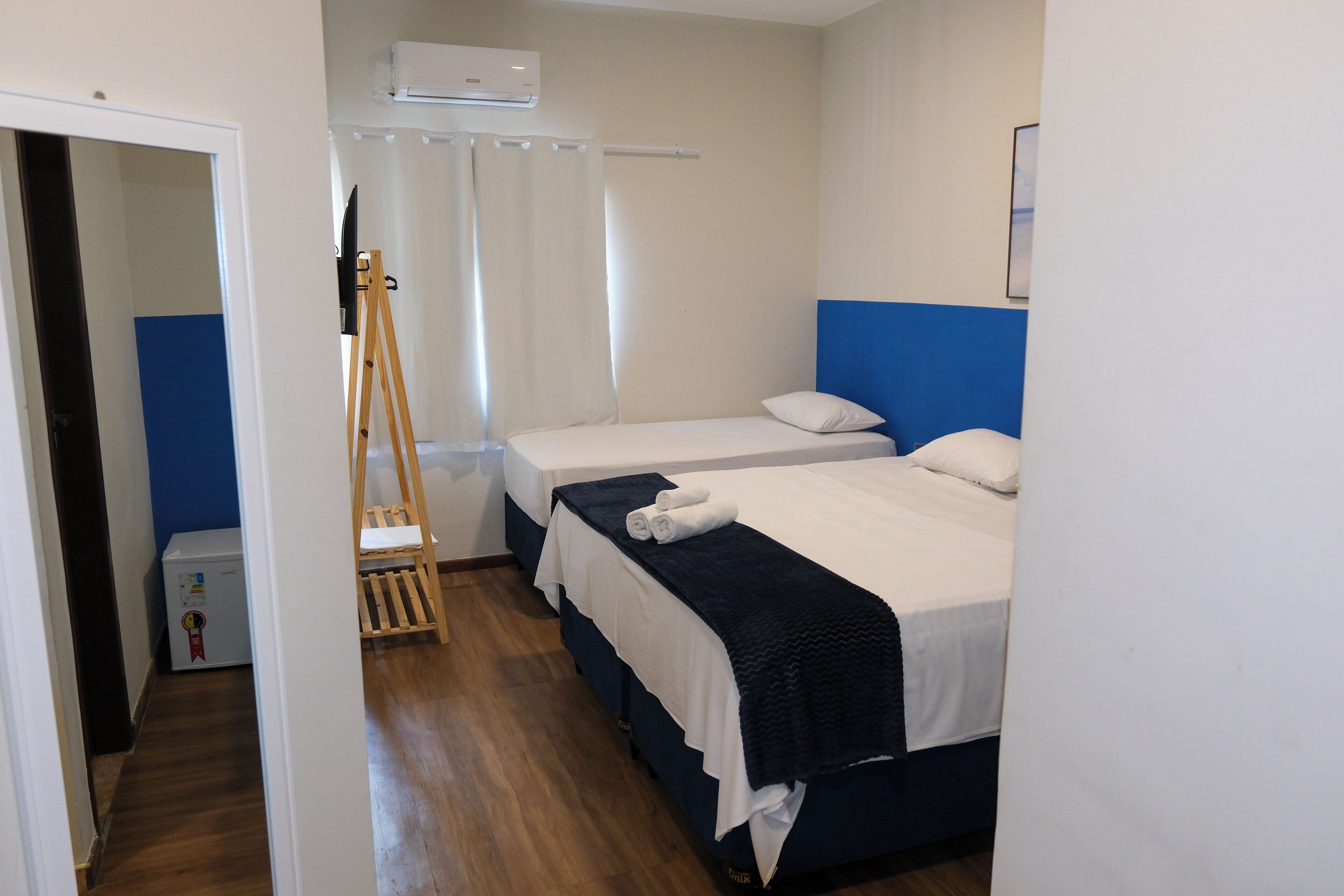 A hotel room with two beds, a wooden ladder, a white air conditioner, and a blue accent wall.