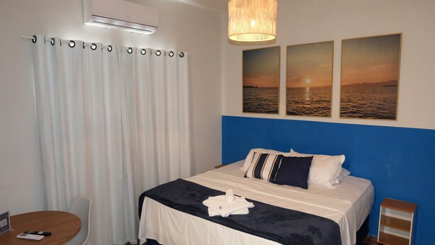Habitación de hotel con cama, escritorio, silla, mesita pequeña y aire acondicionado instalado en la pared.