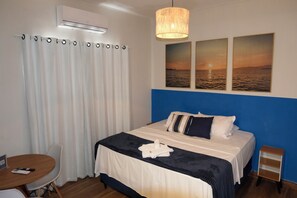 A hotel room with a bed, a desk, a chair, a small table, and a wall-mounted air conditioner. - Pousada Barra Comfort  (Salvador)