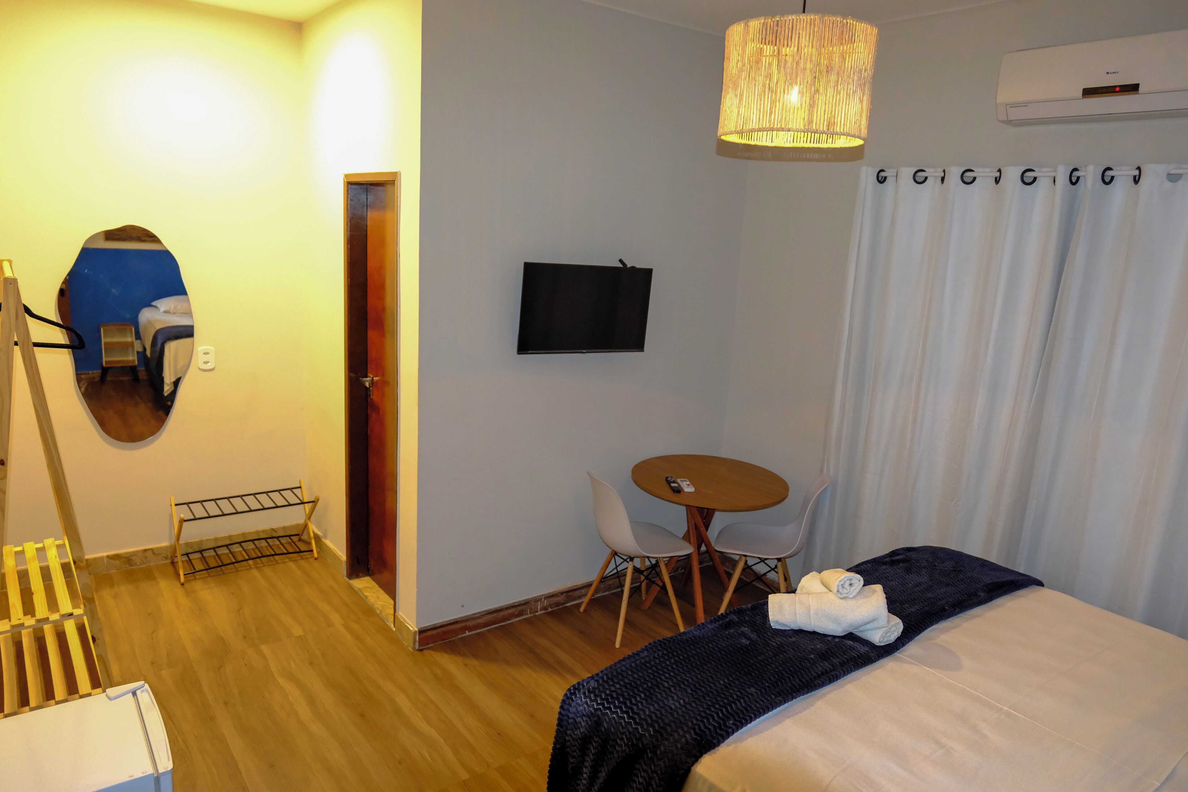 Habitación de hotel con cama, escritorio, silla, televisor y espejo.