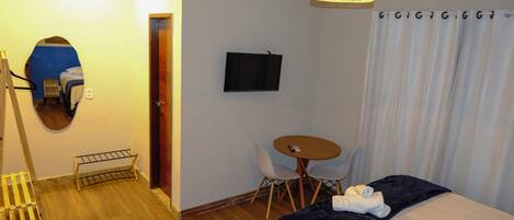 Habitación de hotel con cama, escritorio, silla, televisor y espejo.