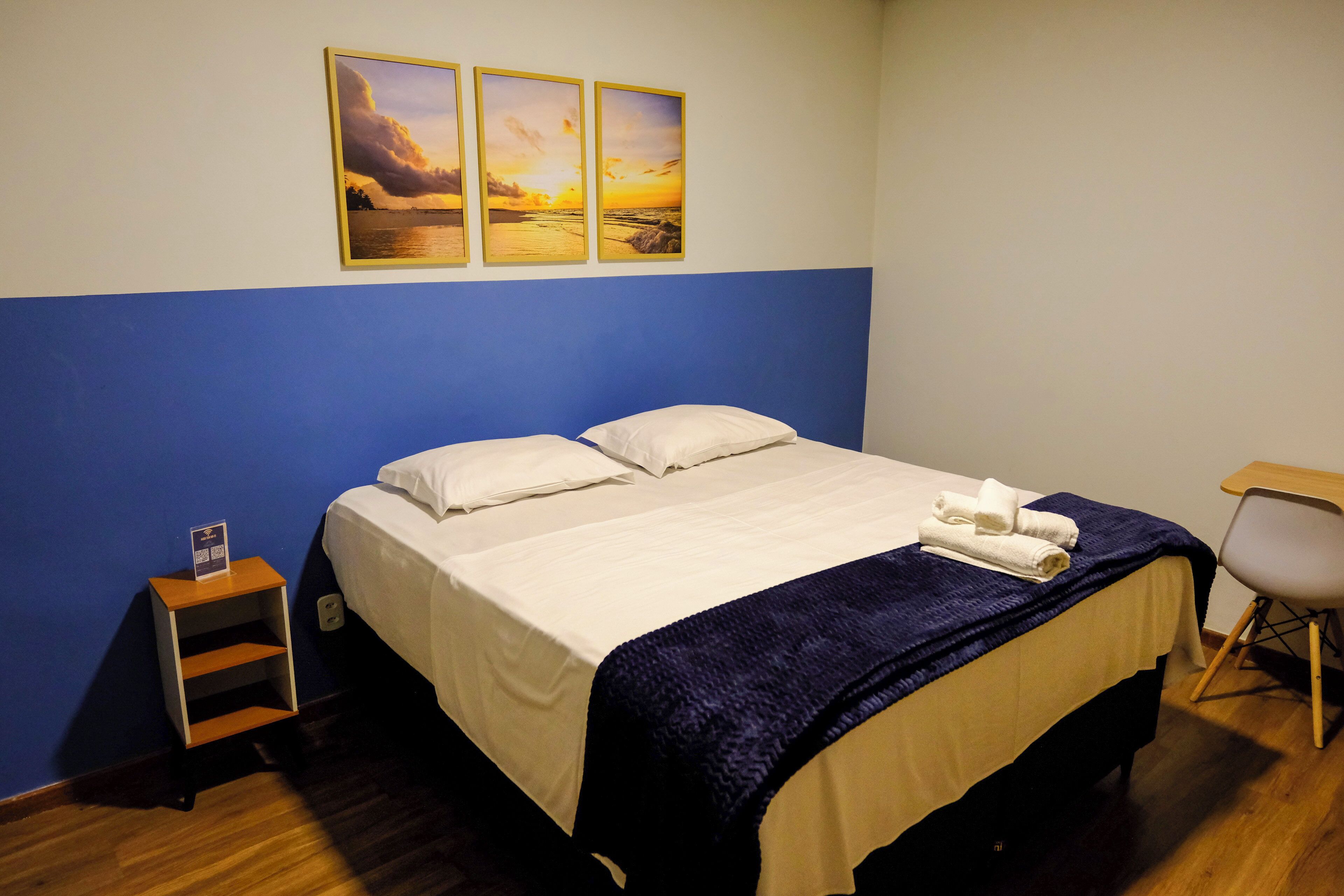 Una habitación de hotel con cama, una silla y tres fotografías del atardecer en la pared.