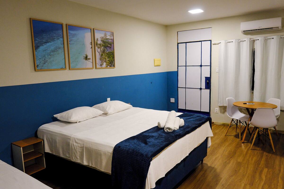 Habitación de hotel con cama, una mesita con sillas y dos cuadros en la pared.