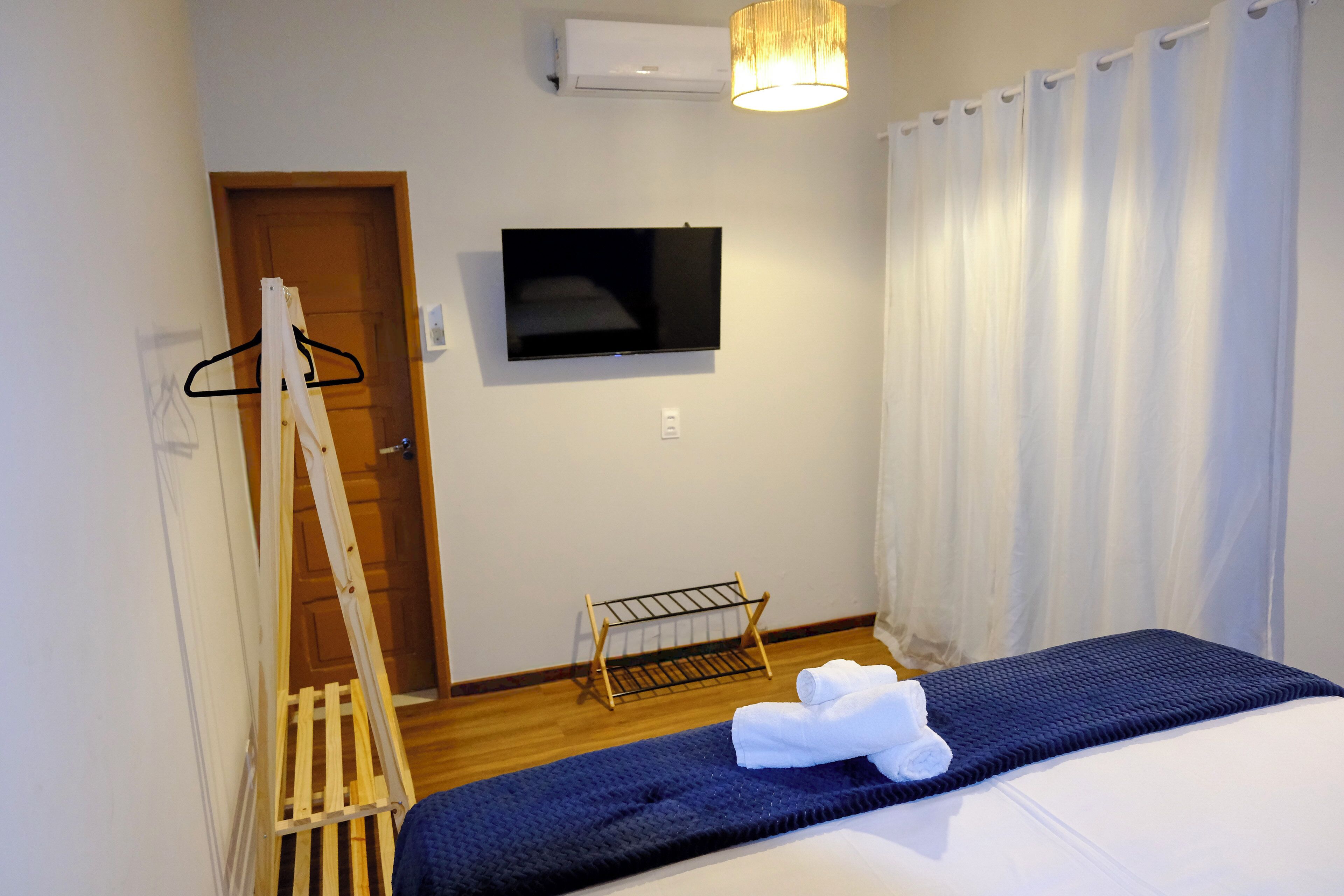 Une chambre avec un lit, une télévision, un étendoir et une porte.